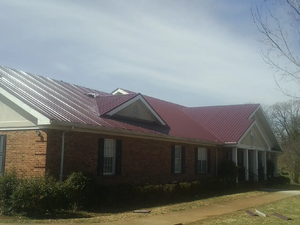 Red metal roof with gabled entries on a long brick building, from a Hail Damage Roof Repair job in Rainsville