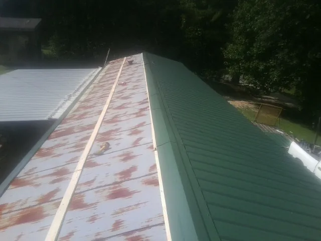 Old rusted panels beside newly installed green metal roofing — Wind Damage Roof Repair by Roofing Brothers in Rainsville