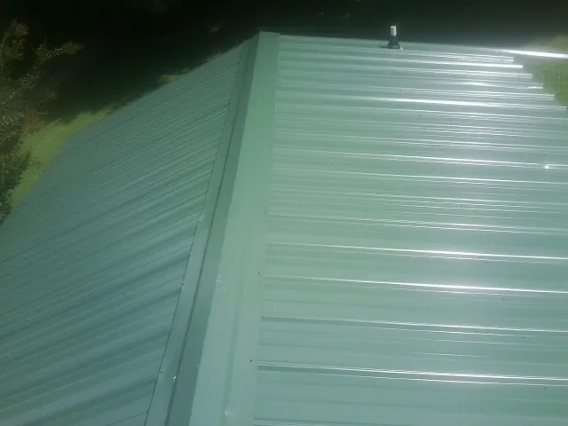New green metal panels meeting at the ridge of a roof — Flat Roof Repair work by our crew in Rainsville
