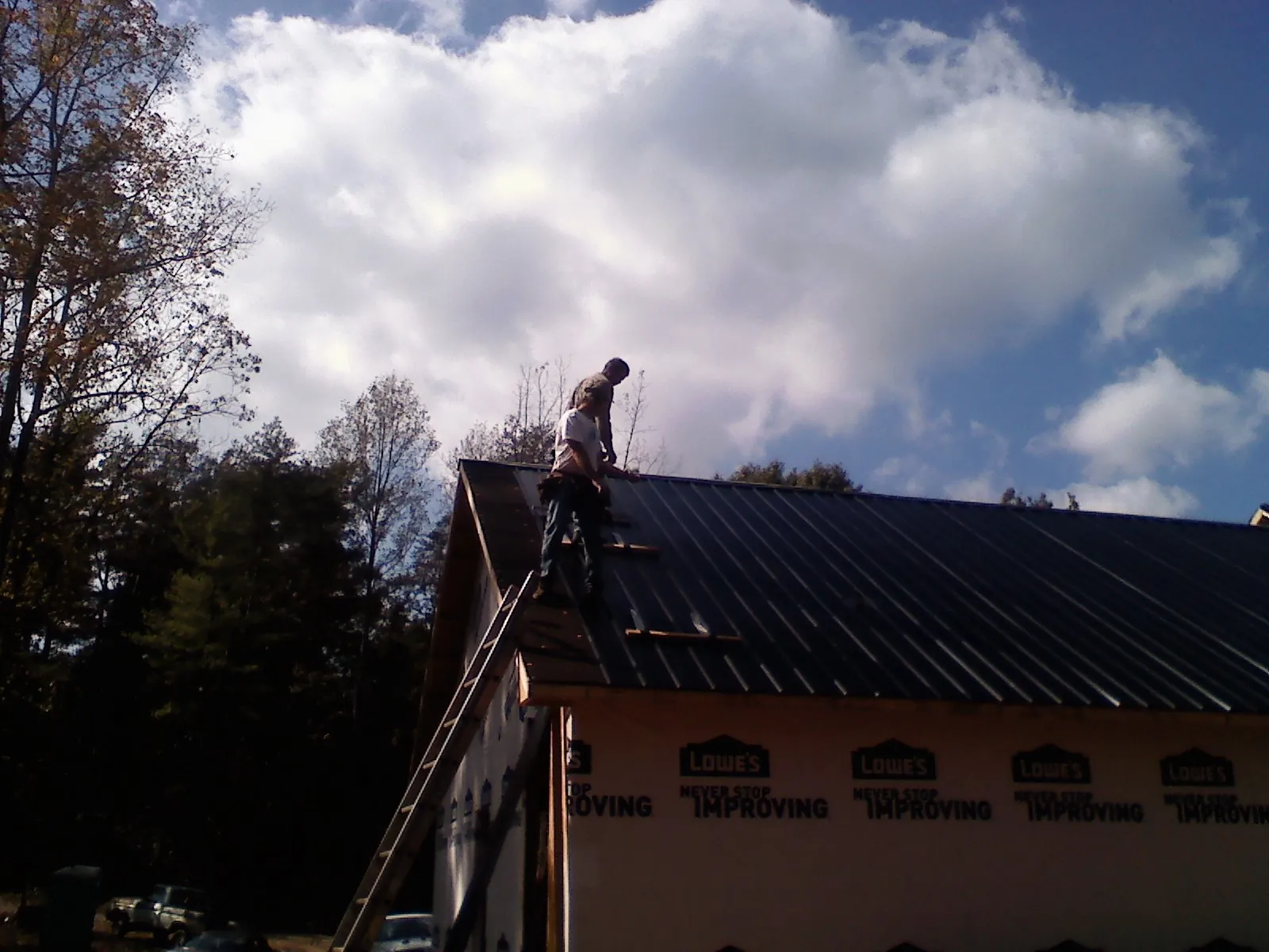 Roofer fastening dark metal panels high against a cloudy sky, from a Roof Inspection job in Rainsville