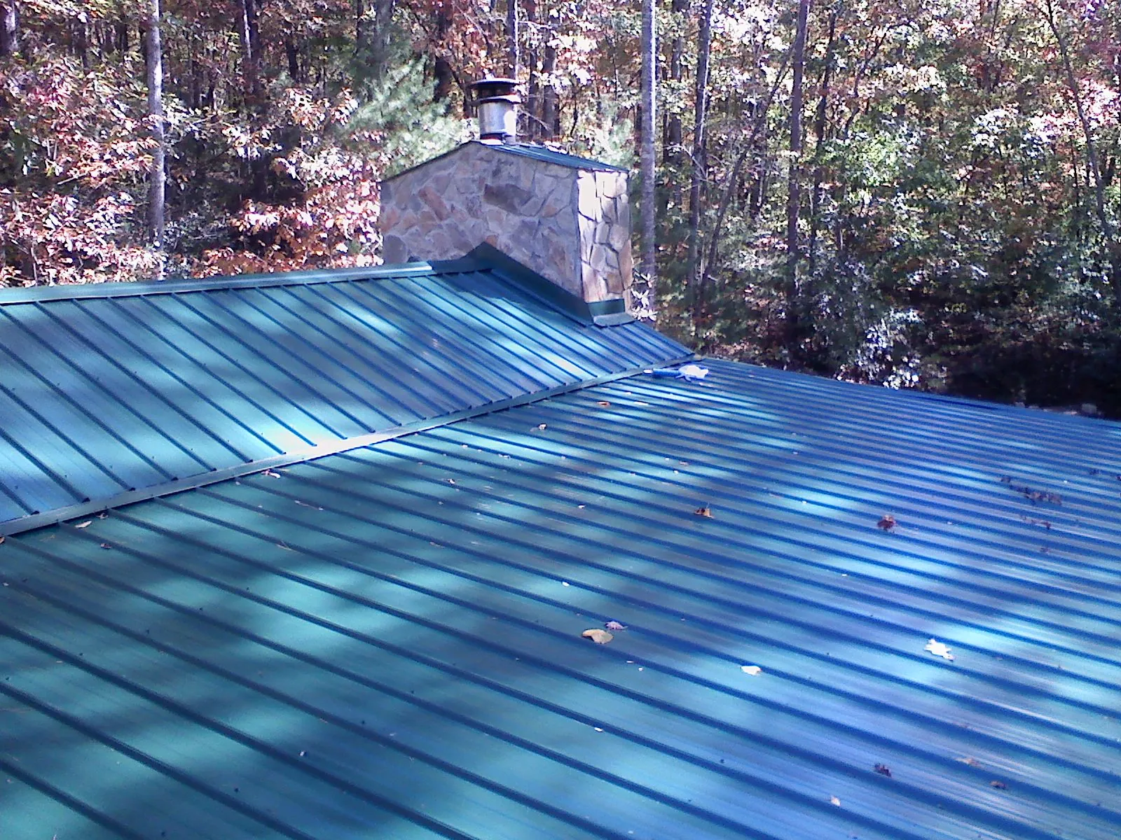 New green metal roof and stone chimney surrounded by autumn woods in Rainsville