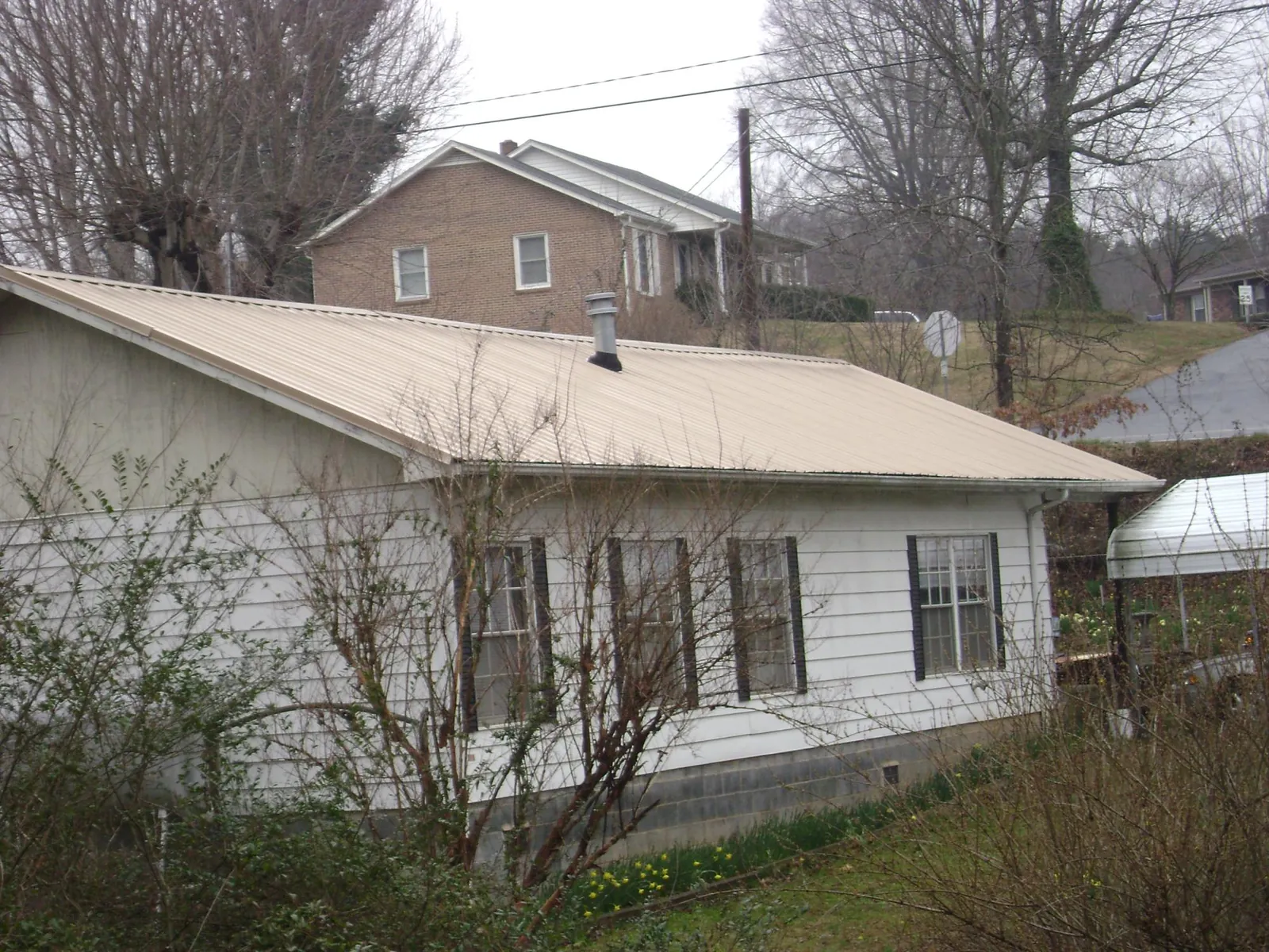 Tan metal roof on a white sided house set into a hillside — Commercial Roofing by Roofing Brothers in Rainsville