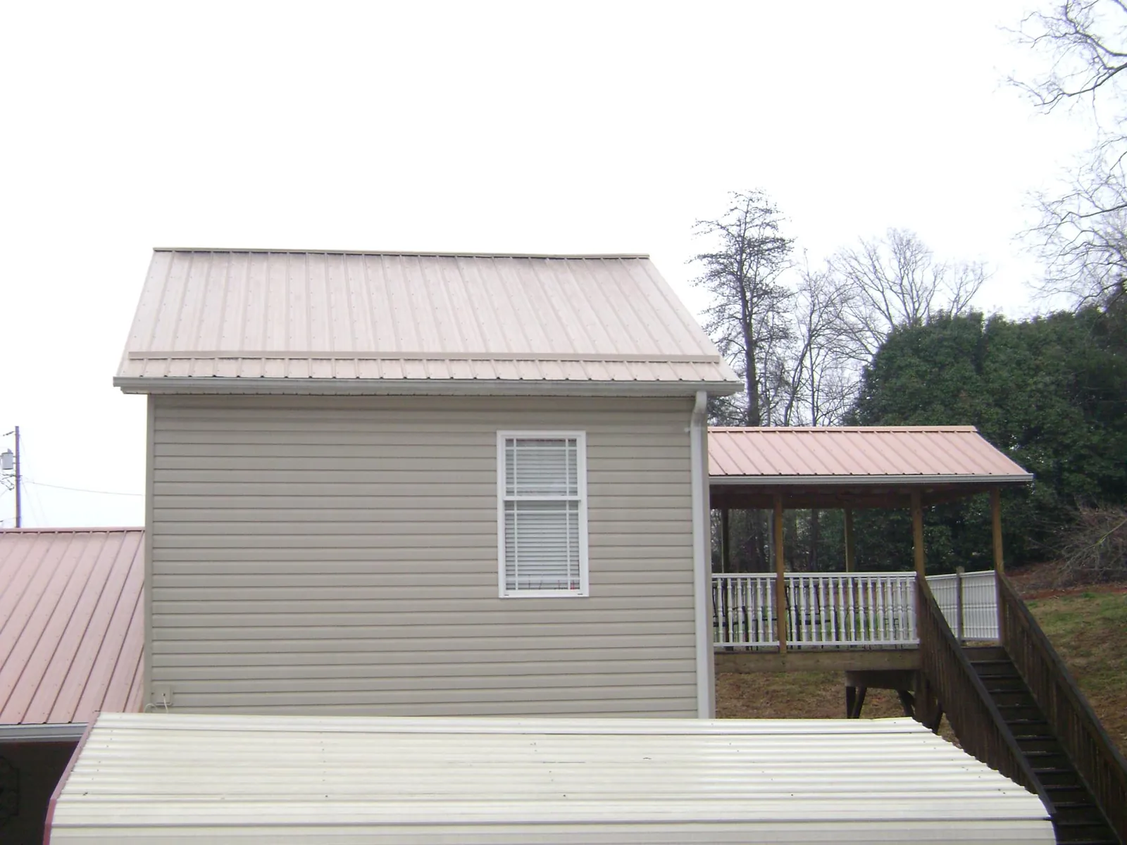 Tan metal roofs on a two story addition and attached porch, from a Roof Replacement job in Rainsville